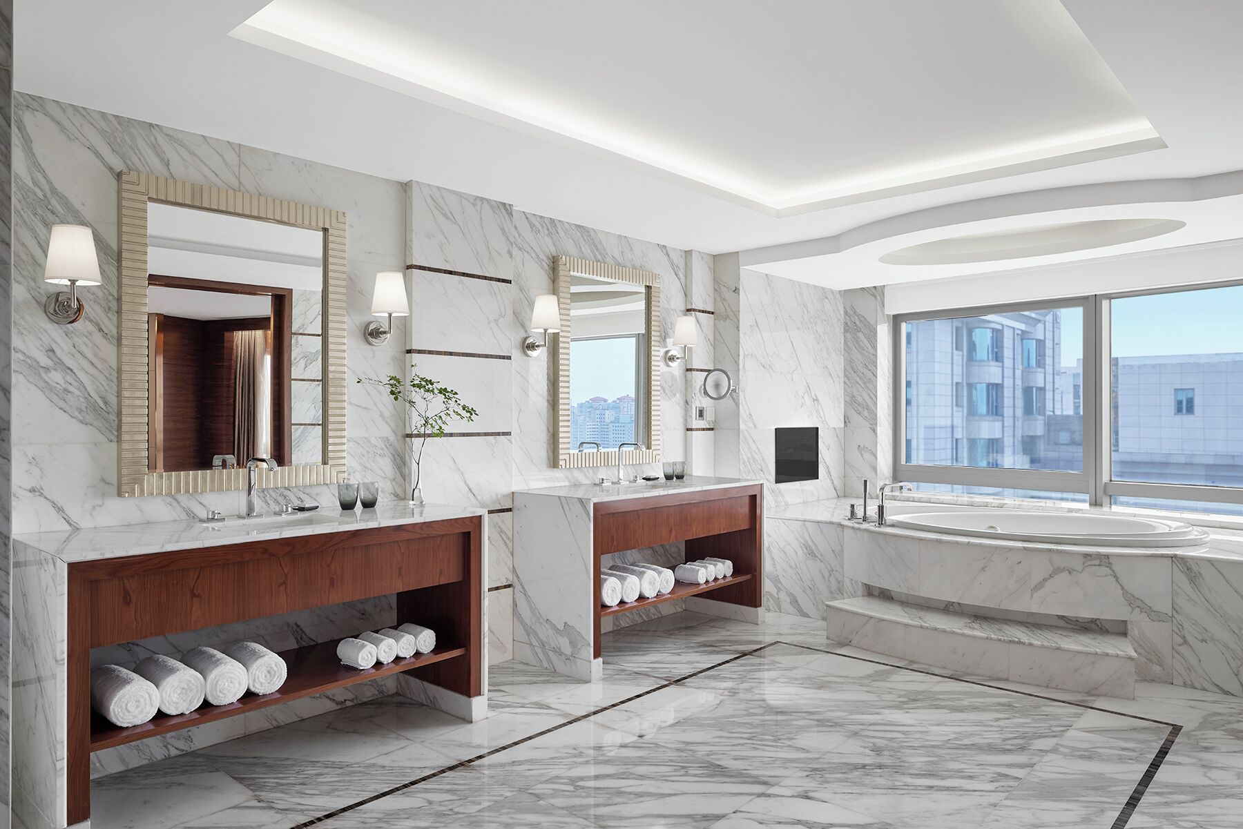 A modern bathroom with marble floors, dual sinks, and a large bathtub.