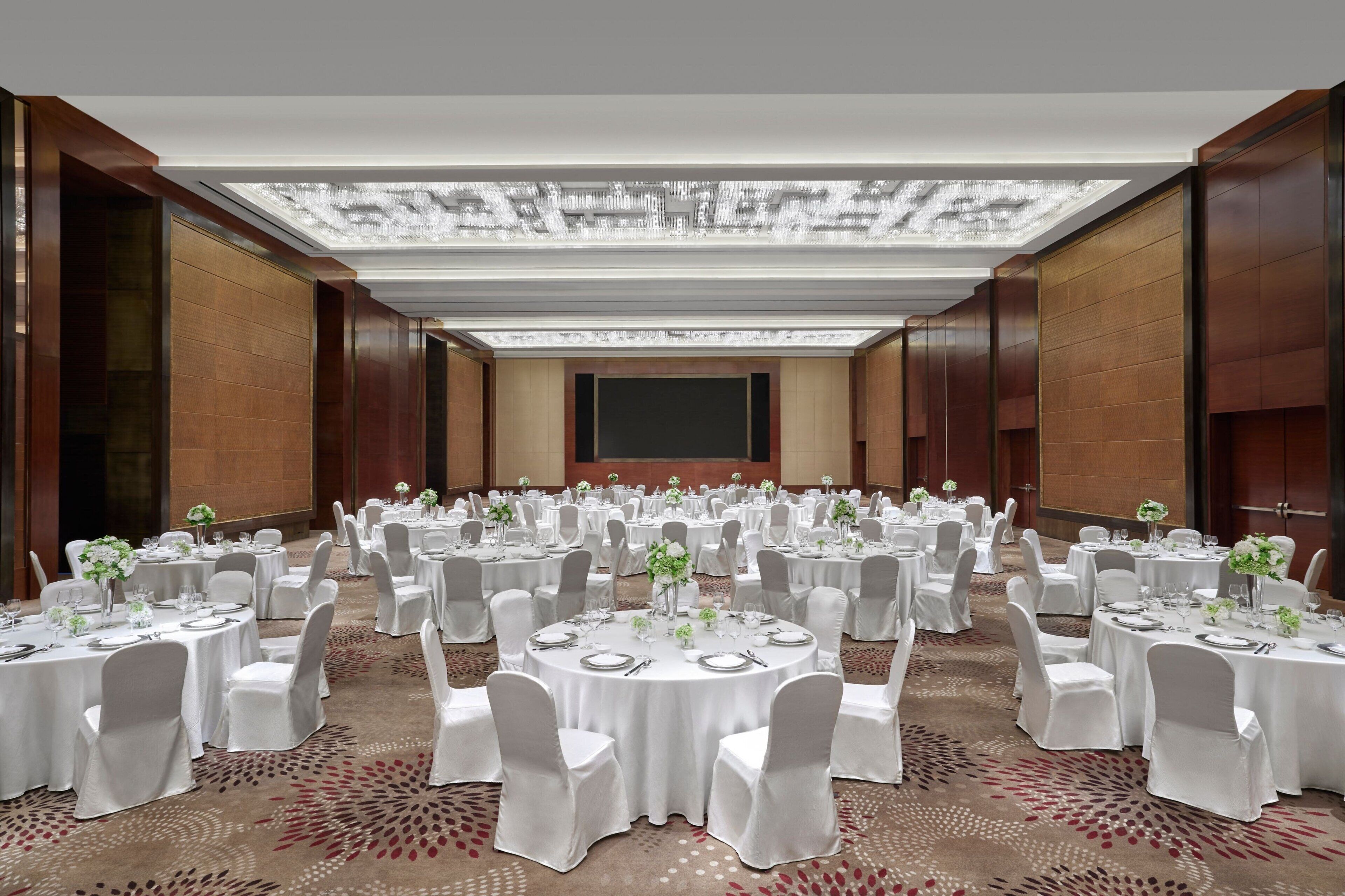 A large banquet hall with round tables, white tablecloths, and chairs.