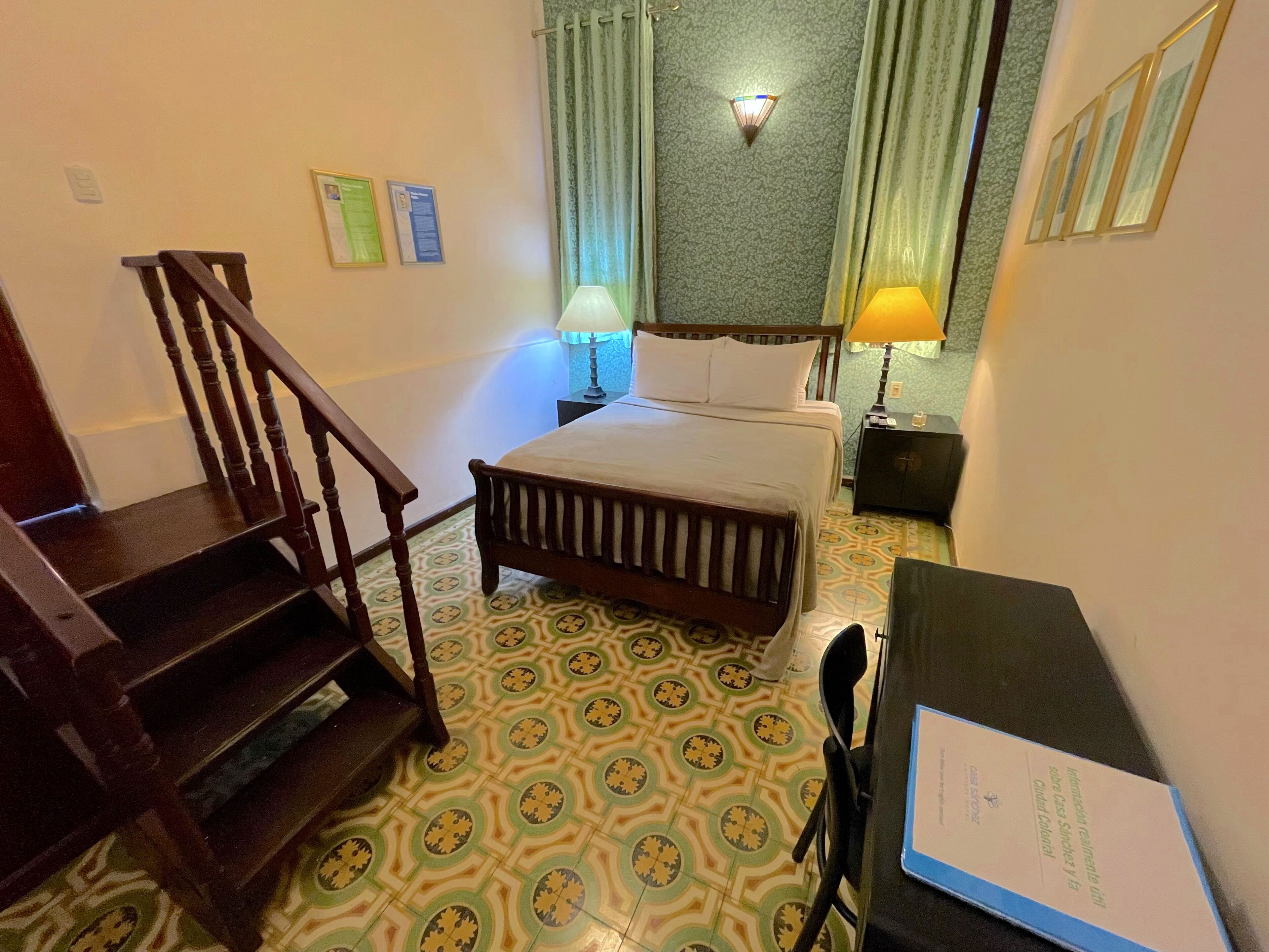 A hotel room with a bed, a desk, a chair, a lamp, and a staircase.