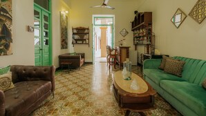Un salon avec un canapé vert, un divan en cuir marron et une table basse en bois. On y trouve également un ventilateur de plafond, une bibliothèque et une porte dont le cadre est vert.