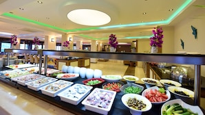 Een buffet met diverse gerechten, een modern interieur, een plafondlamp en decoratieve planten.