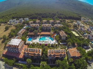 Une vue aérienne d’un complexe hôtelier comprenant plusieurs bâtiments, une piscine centrale et un toboggan aquatique.