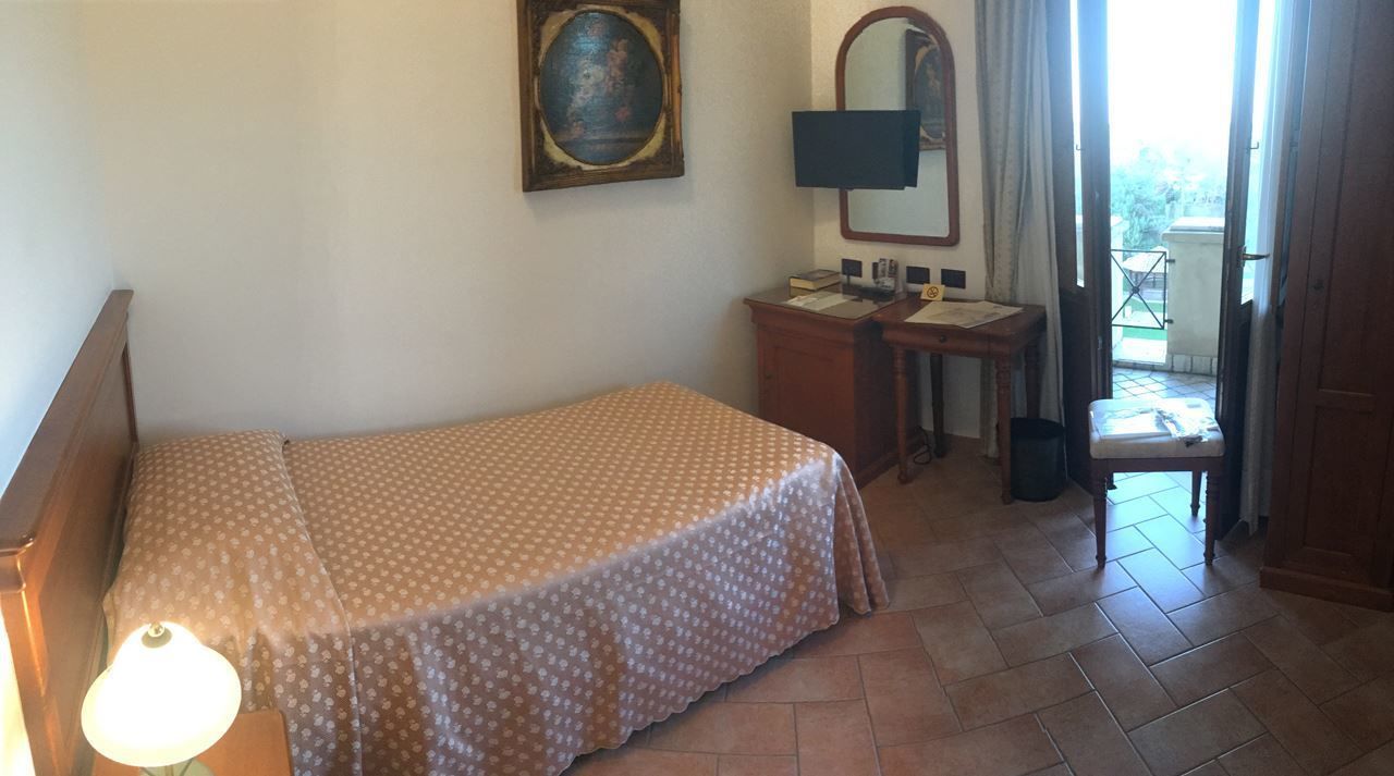 A bedroom with a bed, a desk, a chair, a lamp, a mirror, and a window.