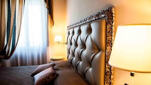 A hotel room with a tufted headboard, a bedside lamp, and a bed with pillows. - Hotel Castello di Septe (Mozzagrogna)