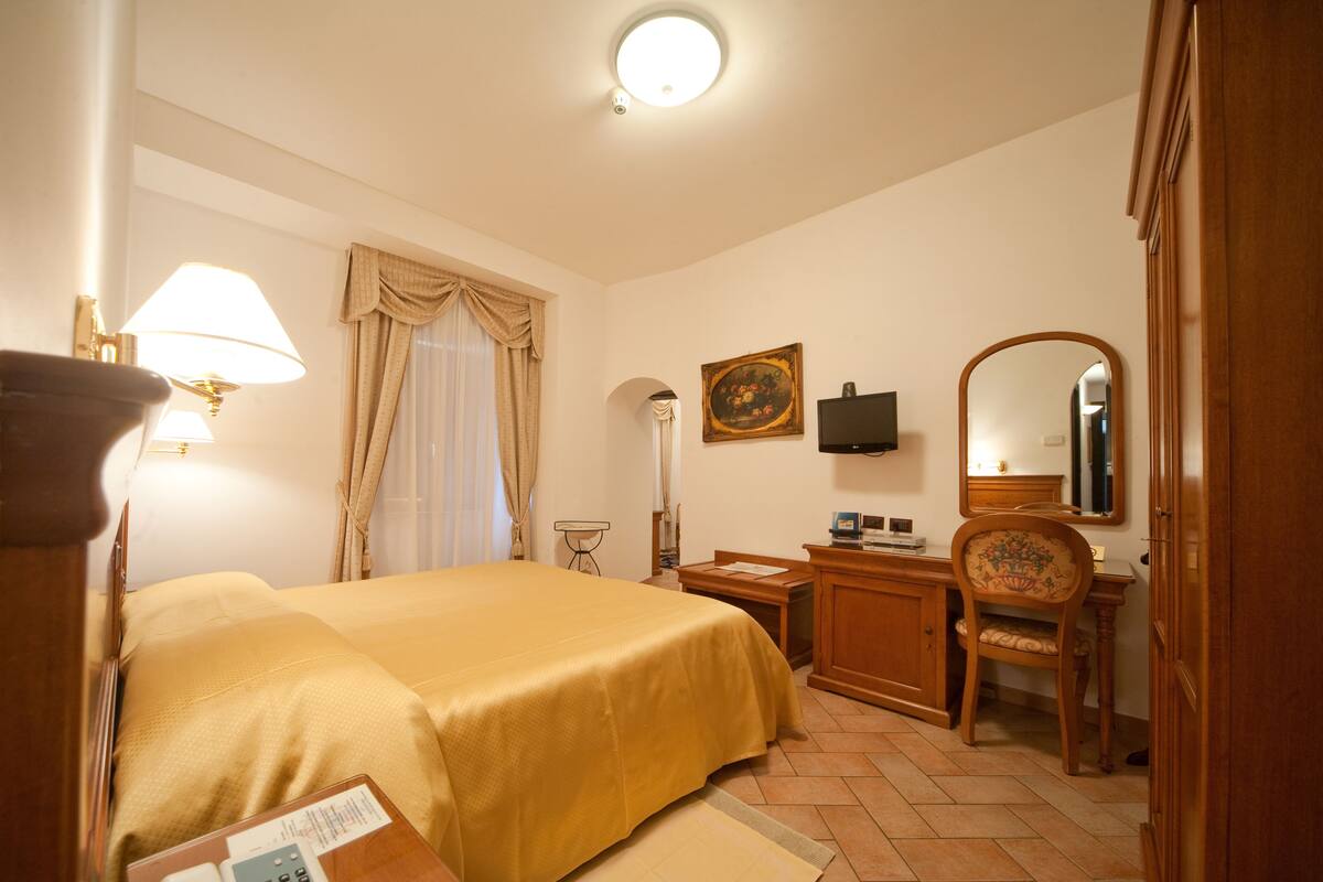 A hotel room with a bed, desk, chair, and a television.
