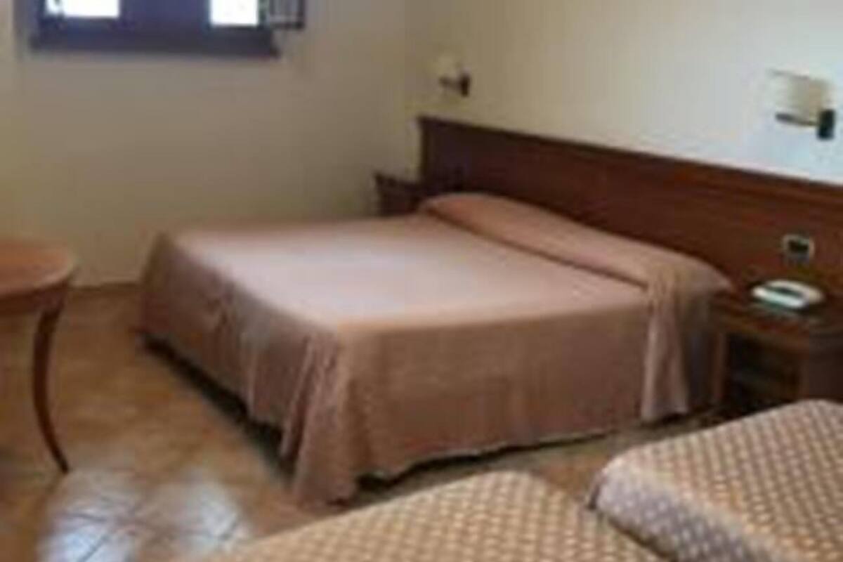 A single-bed room with a wooden headboard, a small bedside table, and a window with a view.