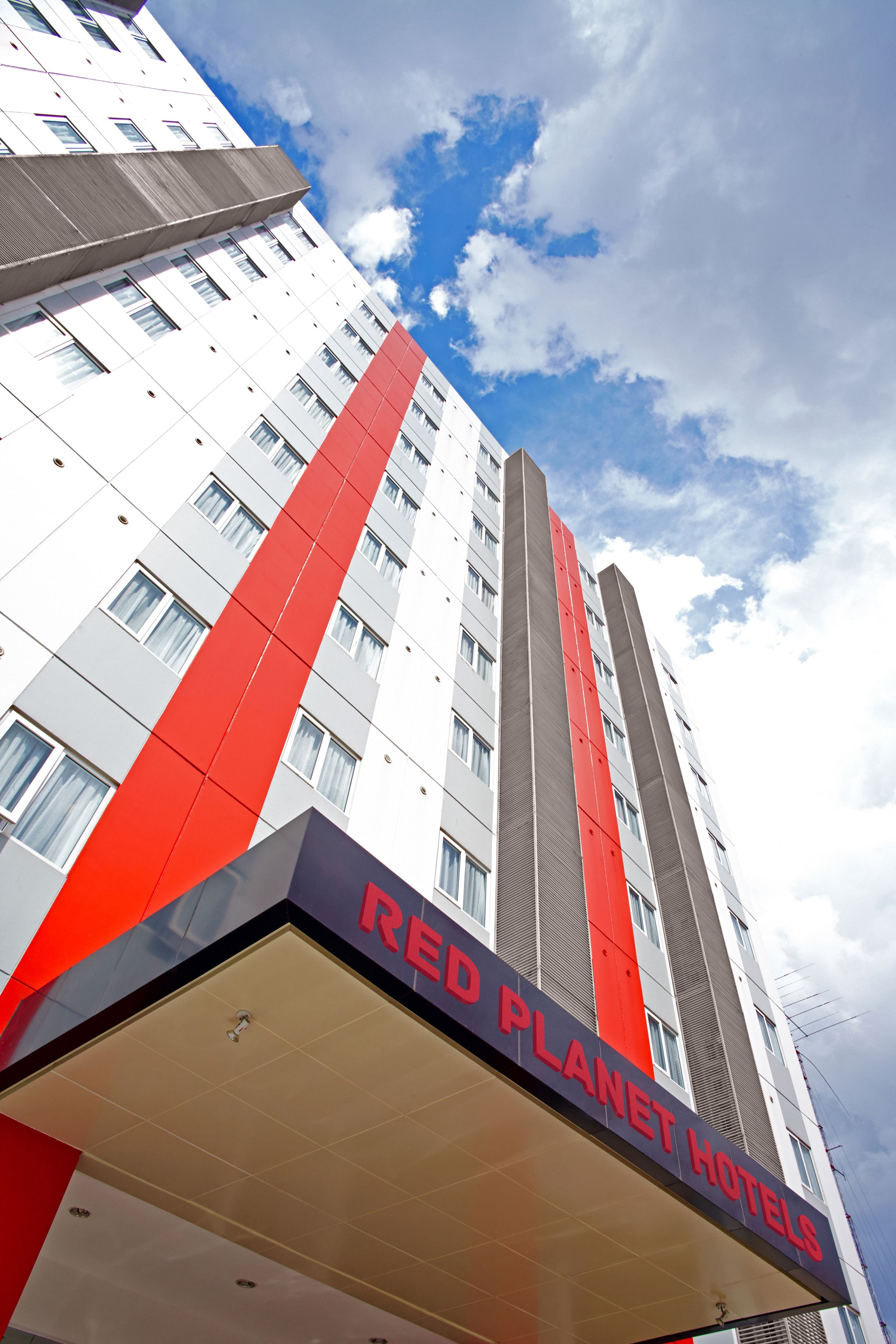 Hotel Red Planet, con un diseño moderno, presenta una fachada prominente en rojo y gris y numerosas ventanas.