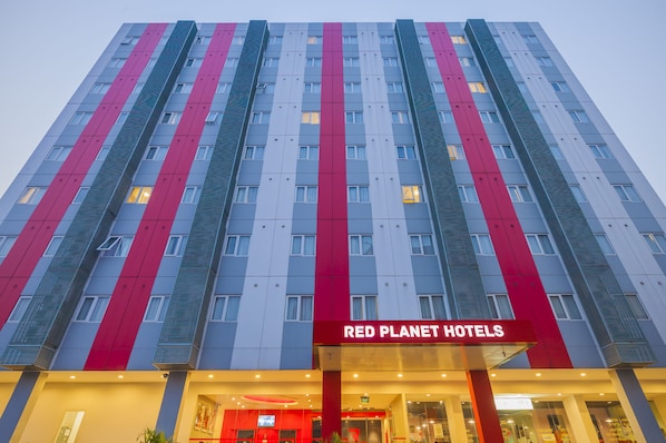 A multi-story hotel with a red and grey facade, featuring the name 'Red Planet Hotels' prominently displayed.
