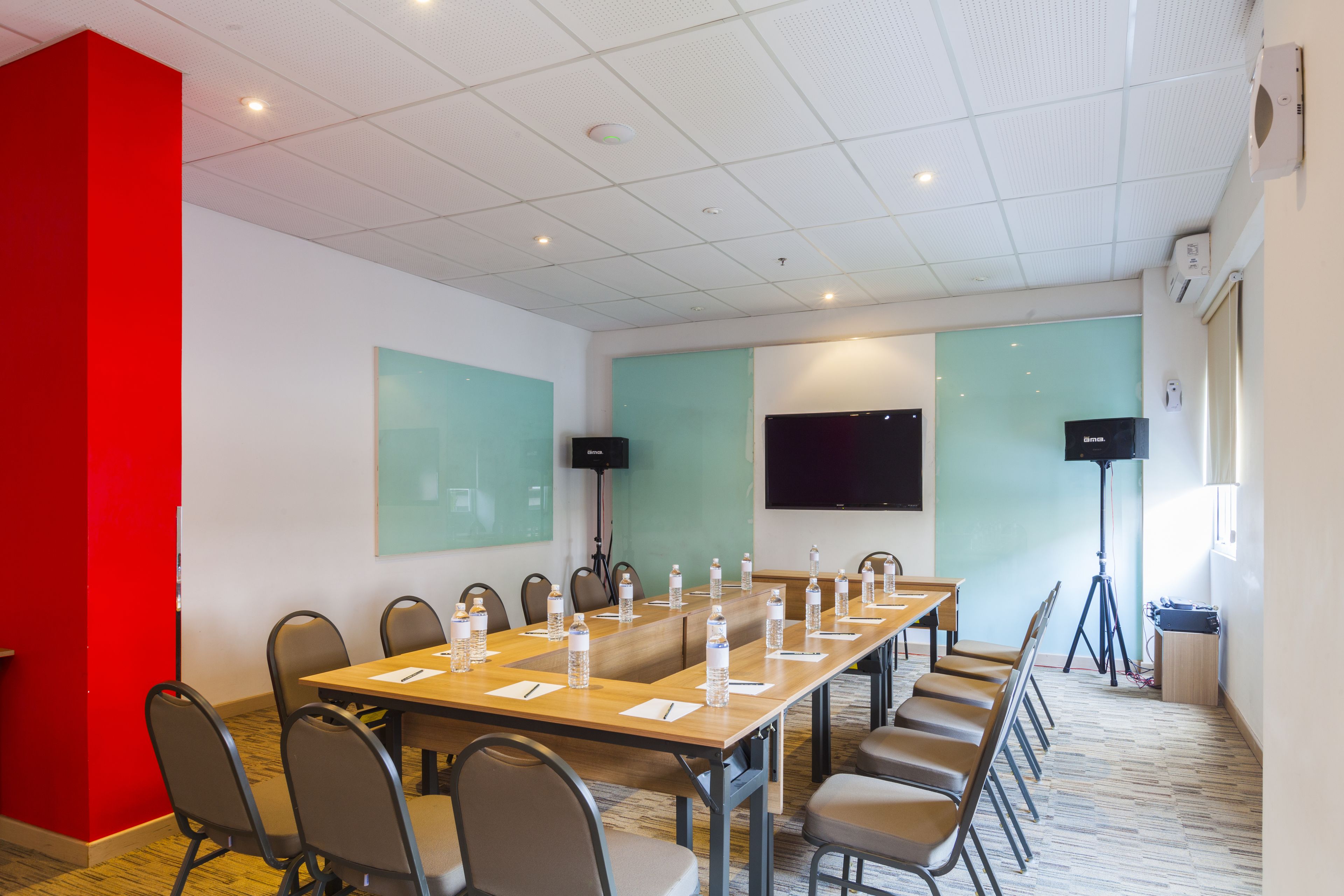 Un salón de conferencias con una larga mesa, sillas, botellas de agua y una pantalla de proyector.