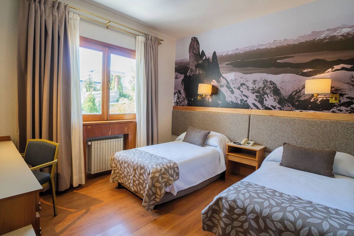 Een hotelkamer met twee bedden, een bureau, een stoel en een groot raam met gordijnen.