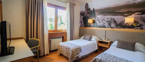 A hotel room with two beds, a desk, a chair, and a large window with curtains.