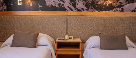 A hotel room with two beds, a nightstand with a telephone, and wall-mounted lamps.