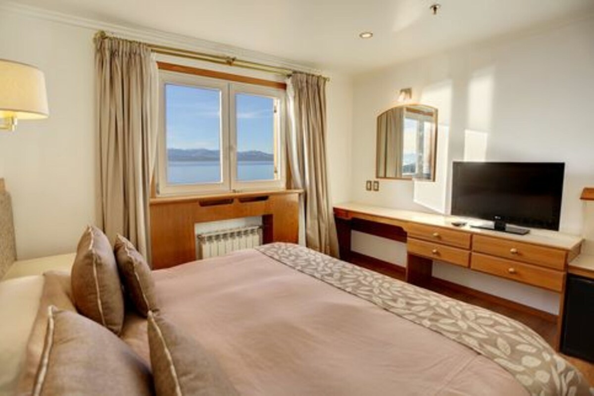 Une chambre d’hôtel avec un lit, une télévision, un bureau et une fenêtre avec des rideaux.