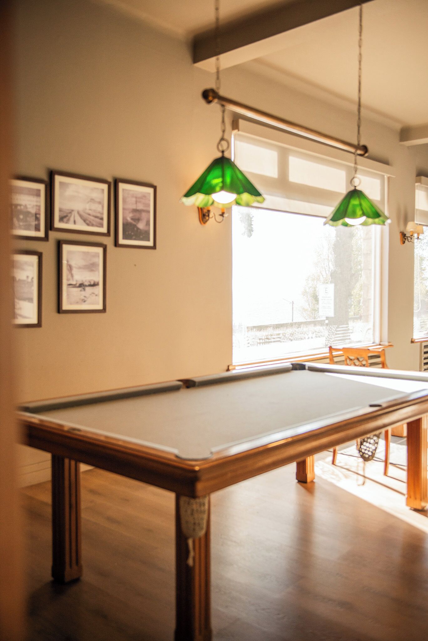 A pool table in a room with framed pictures on the wall and hanging green lamps.