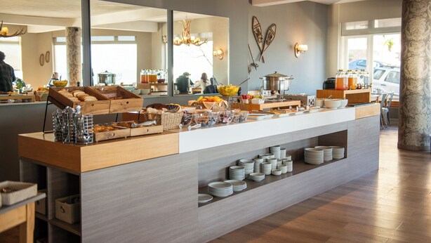 Een buffetopstelling met diverse gerechten en bestek, een spiegel die de ruimte weerspiegelt, en uitzicht op buiten.