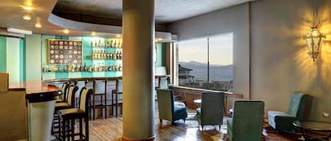 A bar area with a view of the sea, wooden flooring, and seating arrangements.