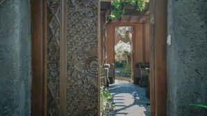 A traditional wooden gate with intricate carvings, leading to a pathway and a garden area. - Parigata Villas Resort (Denpasar)