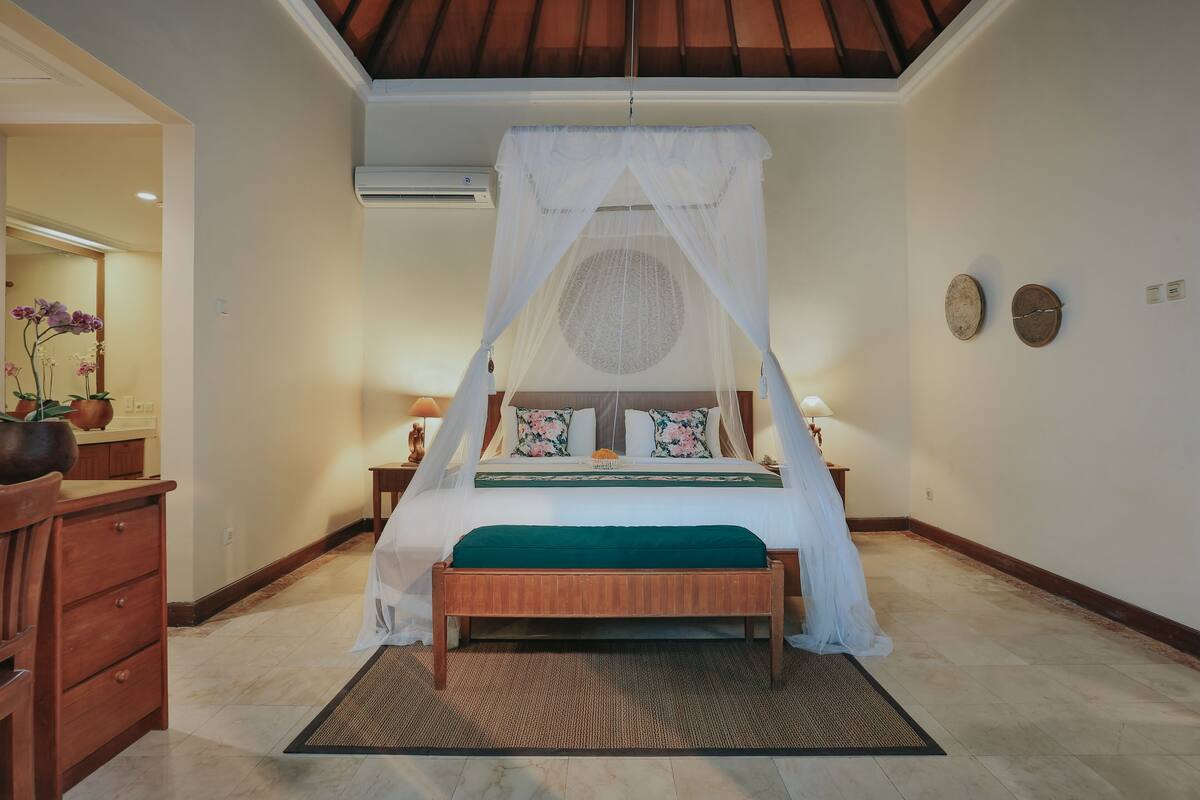 A bedroom with a canopy bed, a wooden nightstand, a bedside table, and a dresser.