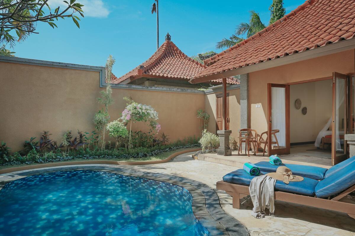 A poolside area with a tiled roof, lounge chairs, and a small garden.