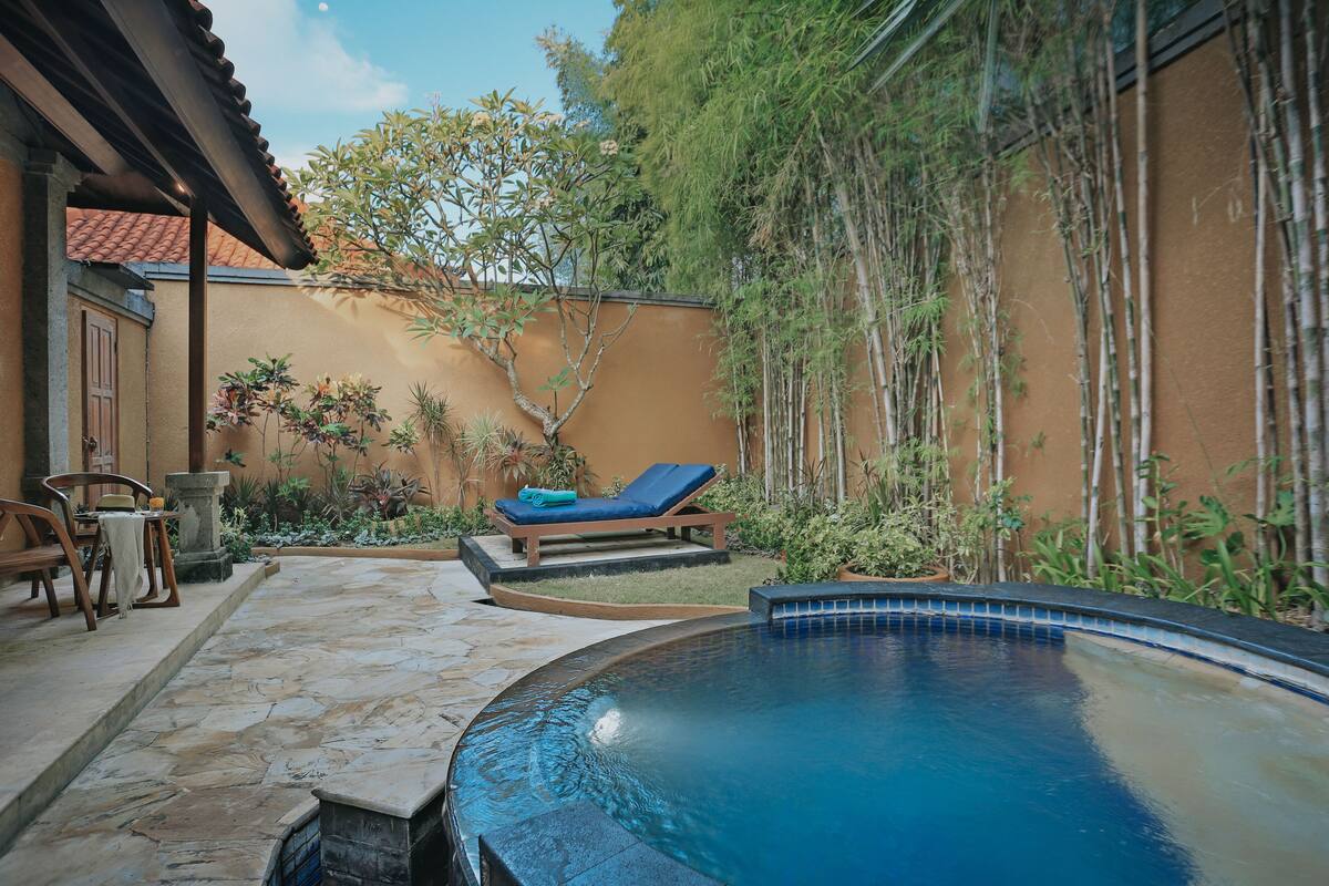 A pool area with a lounge chair, stone flooring, and bamboo plants.