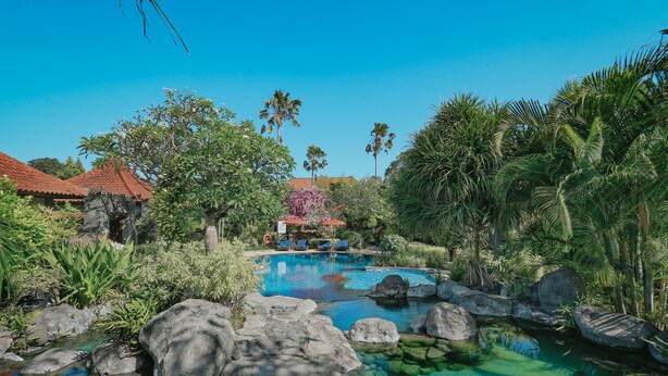 A clear pool surrounded by rocks and tropical plants, with a building in the background. - Parigata Villas Resort (Denpasar)