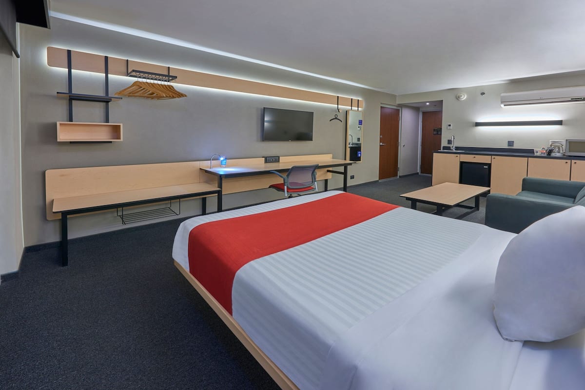 Een hotelkamer met een groot bed, een bureau, een stoel, een televisie, een minibar en een kitchenette.