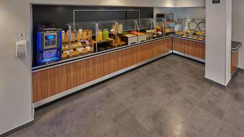 A buffet area with a self-service beverage station, a variety of food options, and a clean, tiled floor.