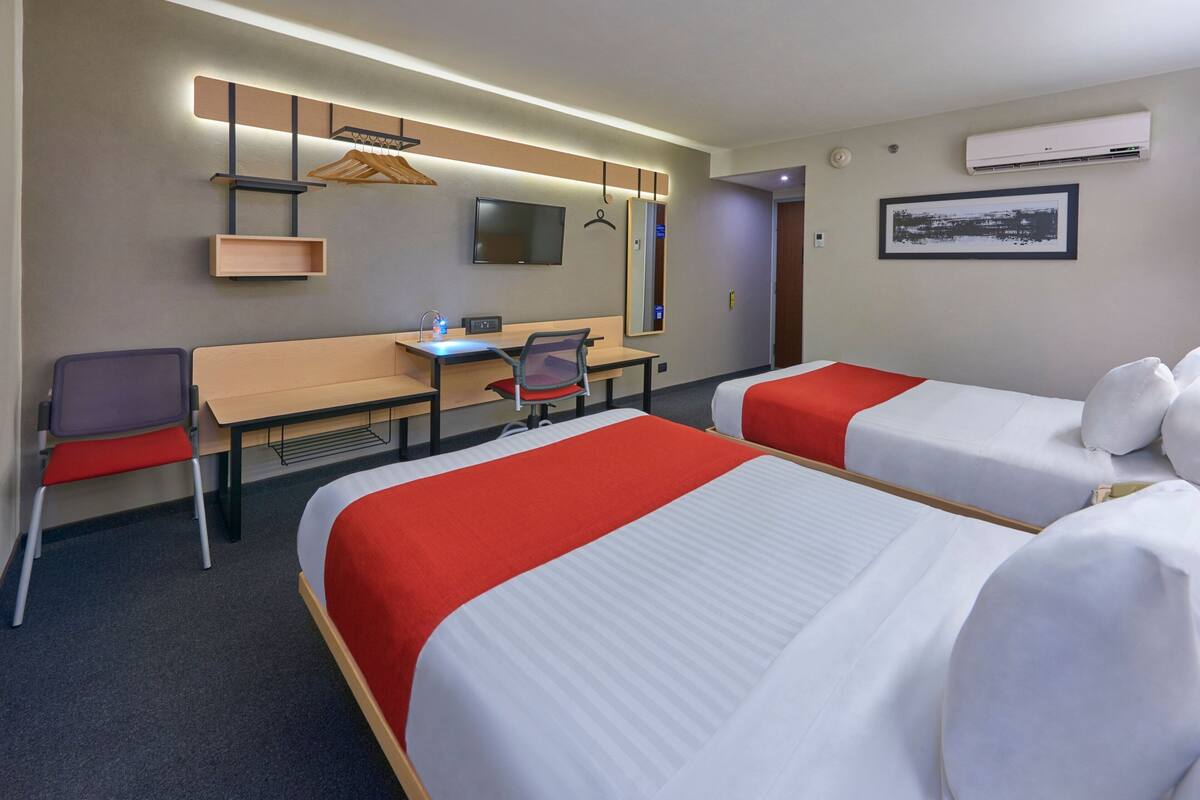 Een hotelkamer met twee bedden, een bureau, een stoel, een televisie en een spiegel.