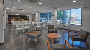 A spacious indoor area with multiple tables and chairs, large windows offering a view of the outside, and a modern ceiling design.