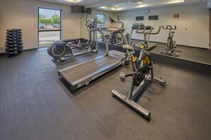 Une salle de sport équipée de machines de cardio, de matériel de musculation et dotée d’un mur entièrement recouvert de miroirs.