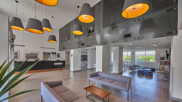 A modern lobby with grey sofas, a wooden coffee table, and black lamps with orange shades.