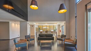 A spacious lobby with a modern design, featuring a central sofa, multiple seating options, and pendant lighting.