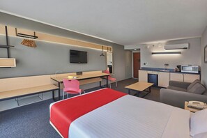 Une chambre d’hôtel comprenant un lit, un bureau, une chaise, une télévision, un coin cuisine et une salle de bain.