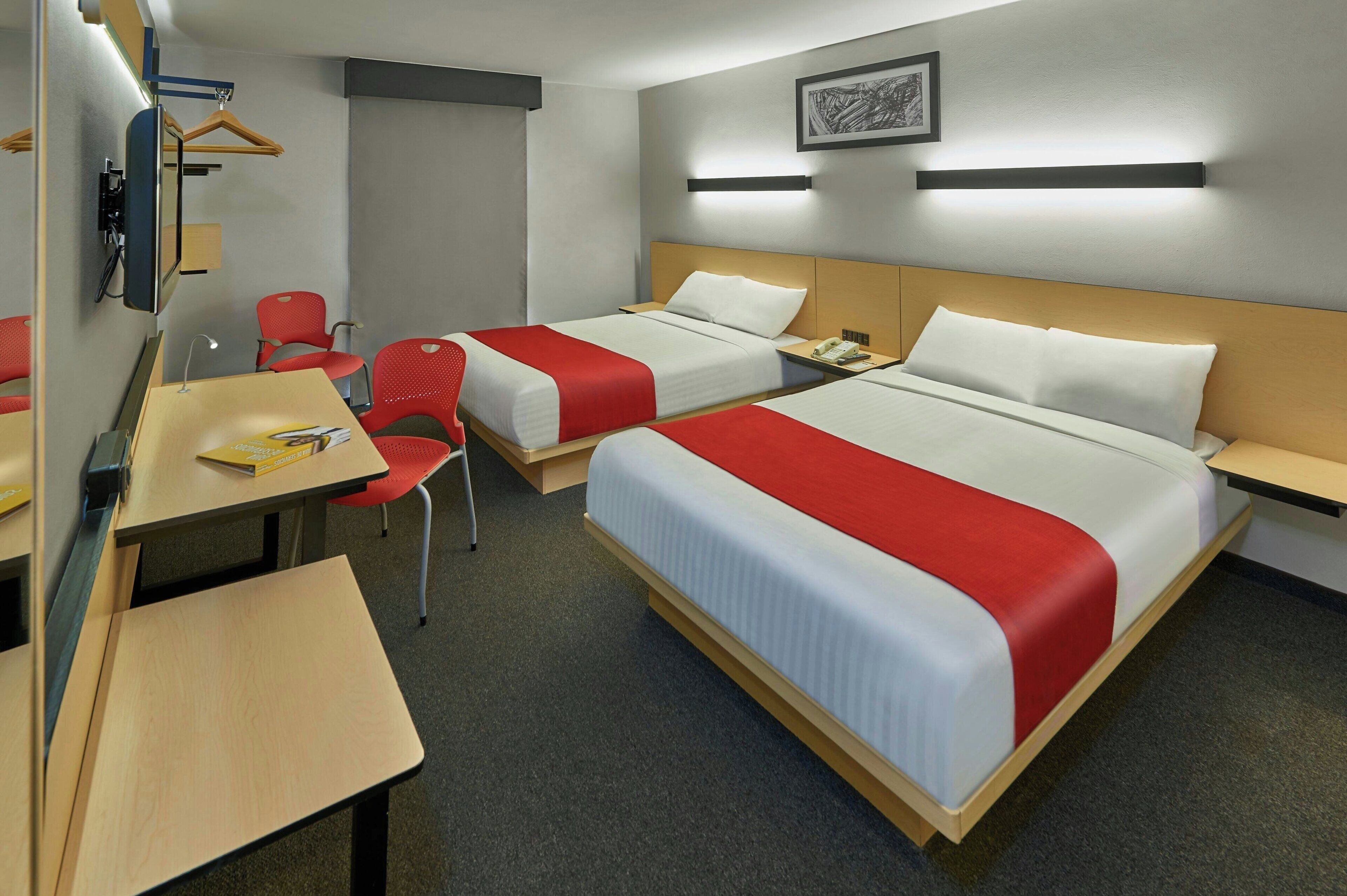 Une chambre d’hôtel avec deux lits, un bureau, une chaise et un téléviseur.