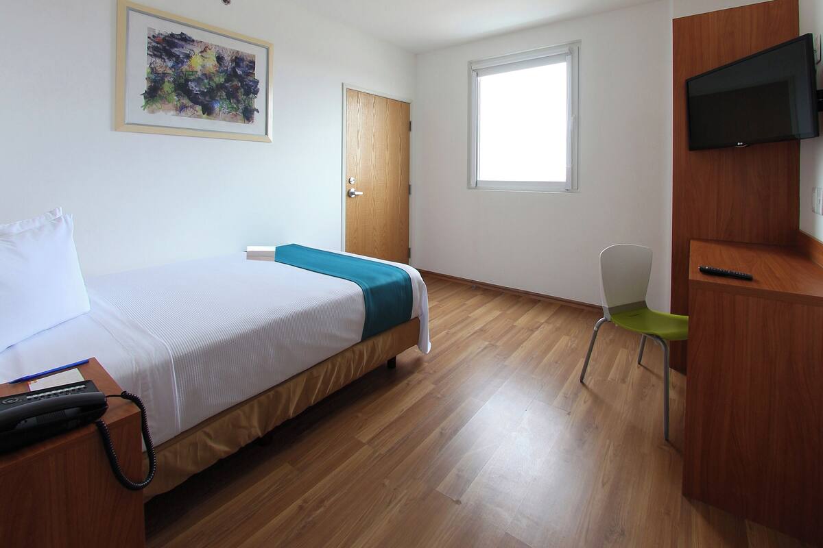 Ein Hotelzimmer mit Bett, Schreibtisch, Stuhl, Fernseher und Fenster.