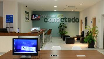 A modern office reception area with a computer monitor, desk, chairs, and a wall-mounted TV.