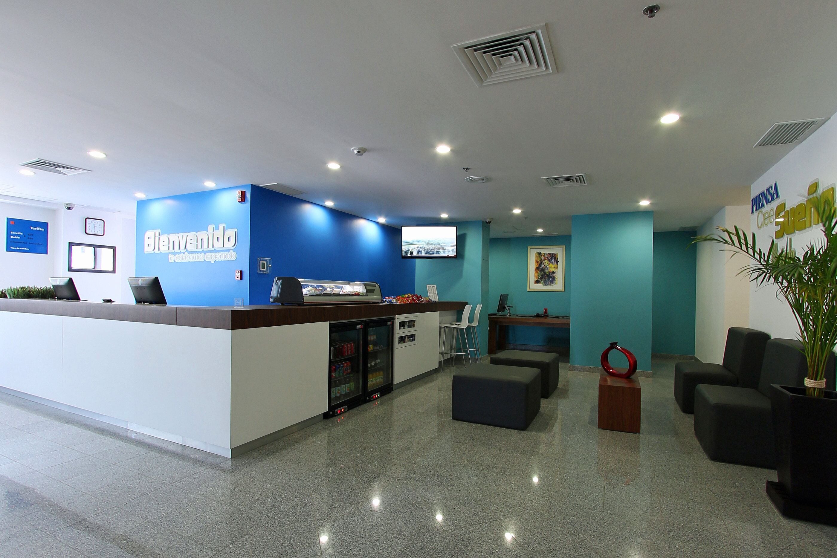 Un área de recepción con pared azul, mostrador, refrigerador, zona de estar y pantalla de televisión.