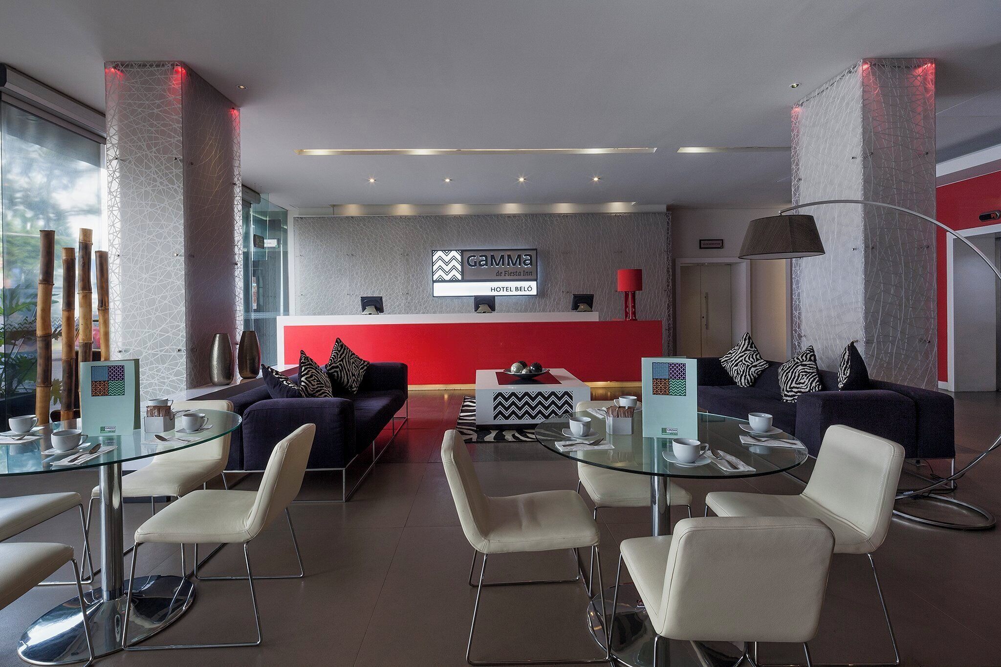 A modern hotel lobby with a reception desk, seating area, and a red accent wall.
