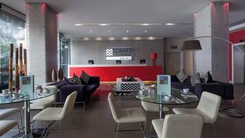 A modern hotel lobby with a reception desk, seating area, and a red accent wall.