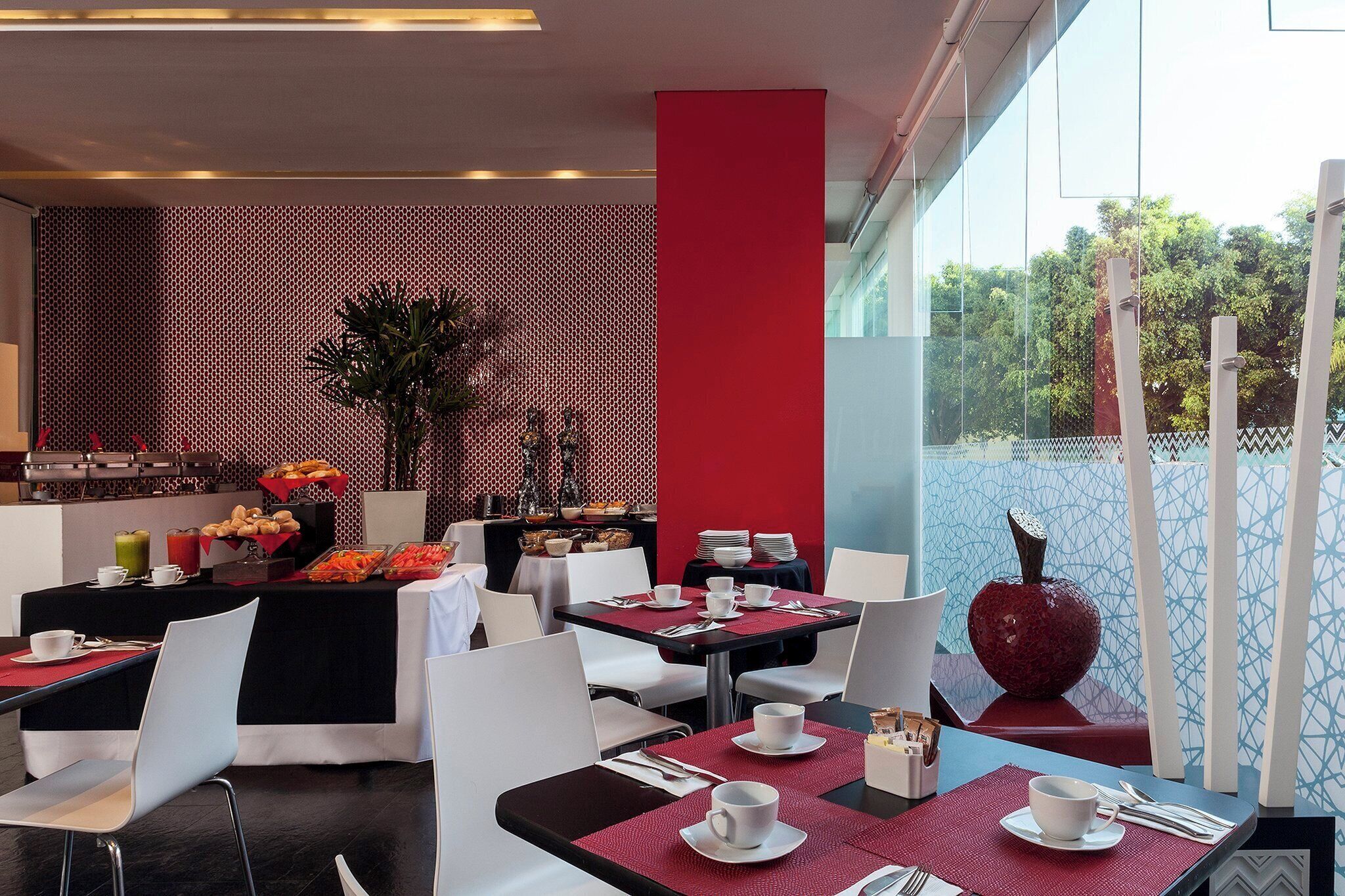 A restaurant with tables set for dining, a buffet with various food items, and a decorative vase.