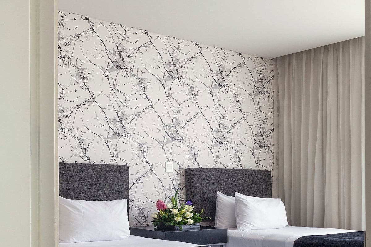 A hotel room with two beds, a marble-patterned wall, a flower arrangement, and a curtain.