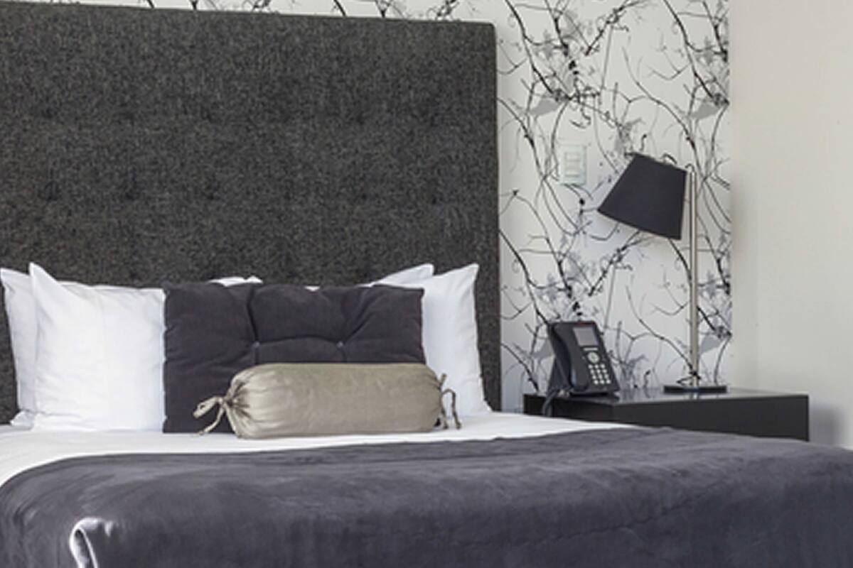 A modern bedroom with a large bed, dark headboard, and a bedside table with a lamp and phone.