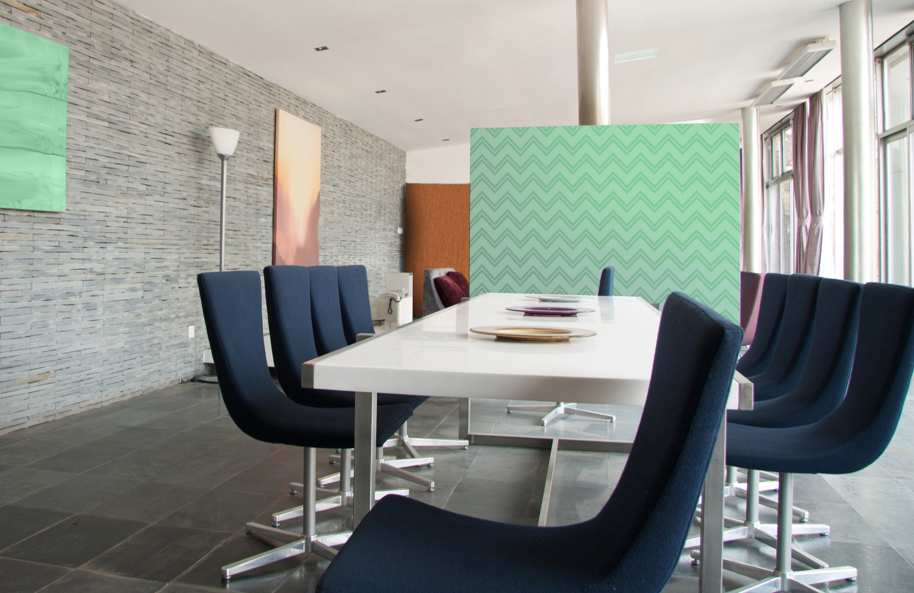 A conference room with a white table, blue chairs, a brick wall, and a green patterned partition.