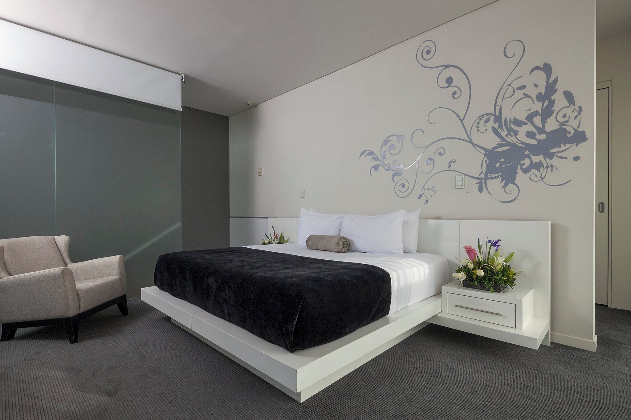 Un dormitorio moderno con una cama, una silla, una mesita de noche y un adorno en la pared.