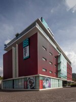 Un edificio moderno con fachada roja, amplios ventanales y señalización de 'Hotel Bello' y 'EVENTOS'.
