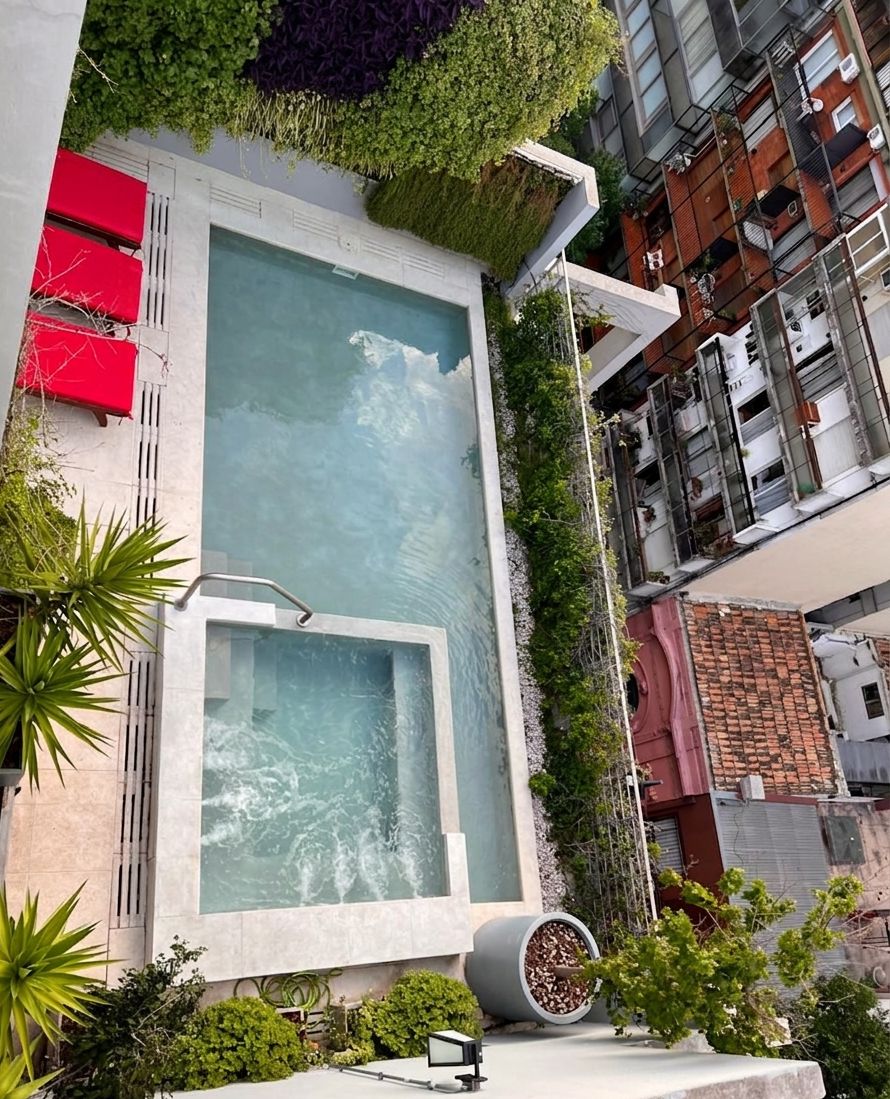 Um edifício moderno com uma piscina retangular, cercada por vegetação e assentos vermelhos.