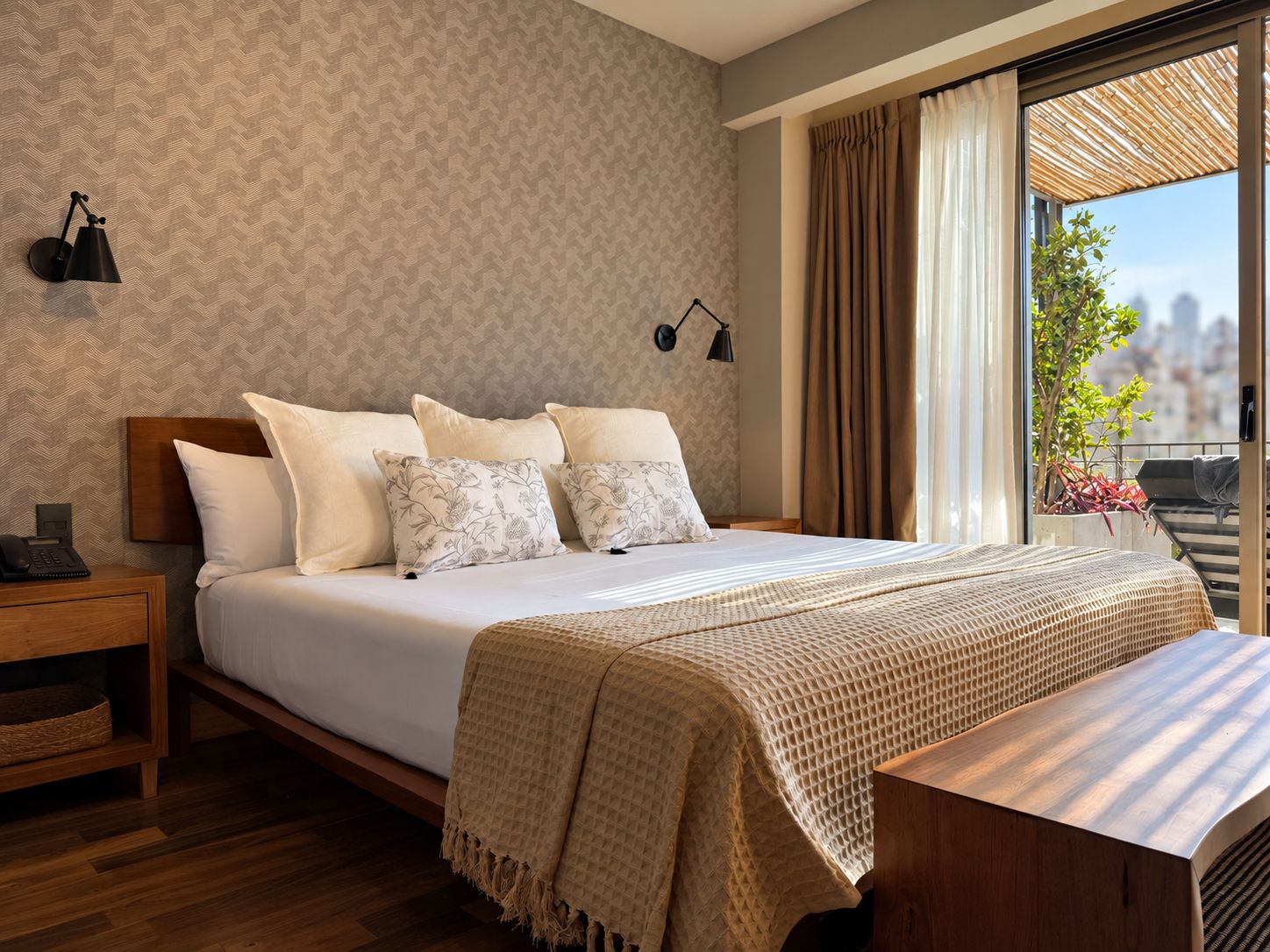 Une chambre d’hôtel moderne avec un grand lit, une table de chevet, une commode, une fenêtre donnant sur la ville et une vue panoramique sur le paysage urbain.