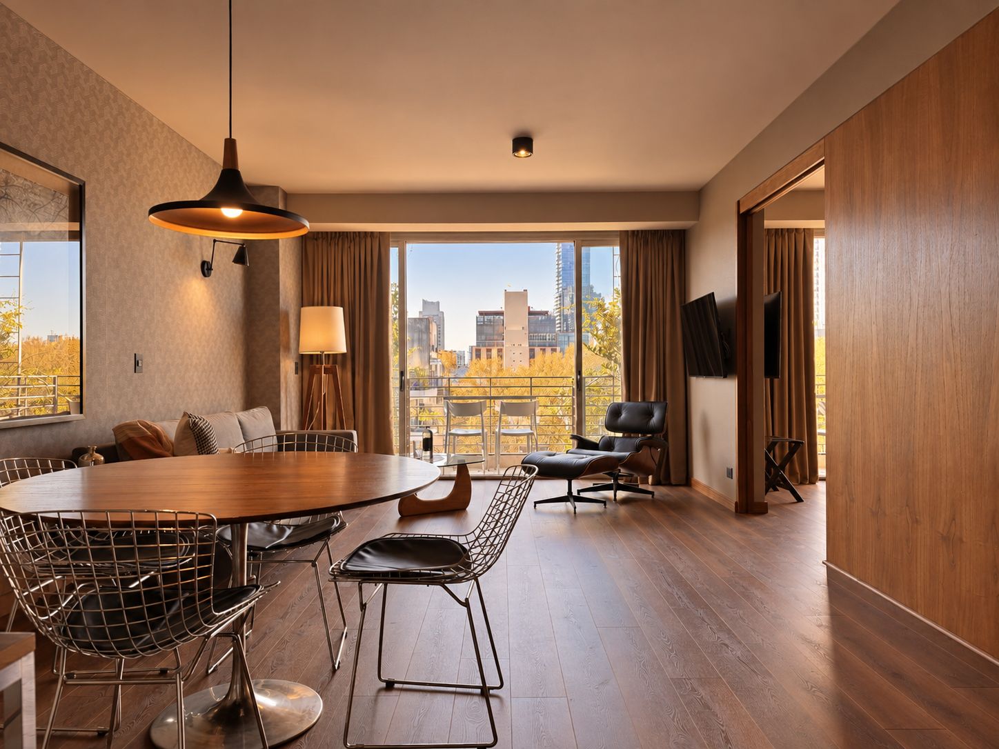 A modern hotel room with a dining area, a sofa, a TV, and a view of the cityscape.