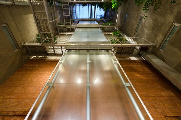 A spacious indoor area with a long, narrow water feature, surrounded by metal railings and potted plants.