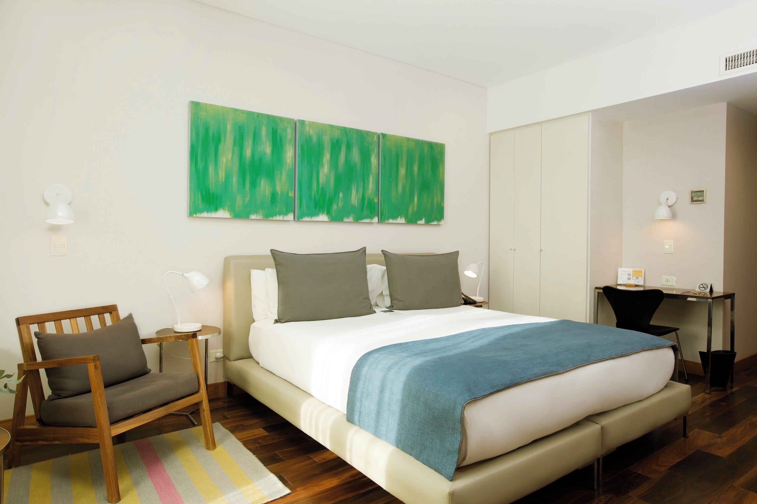 Une chambre d’hôtel moderne avec un grand lit, un bureau, une chaise et un tableau abstrait vert accroché au mur.